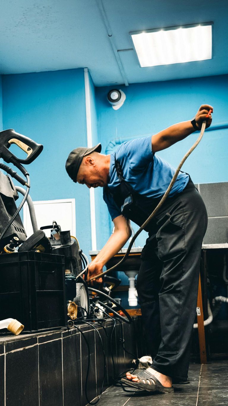 A technician in blue attire repairing equipment in an indoor workshop setting.